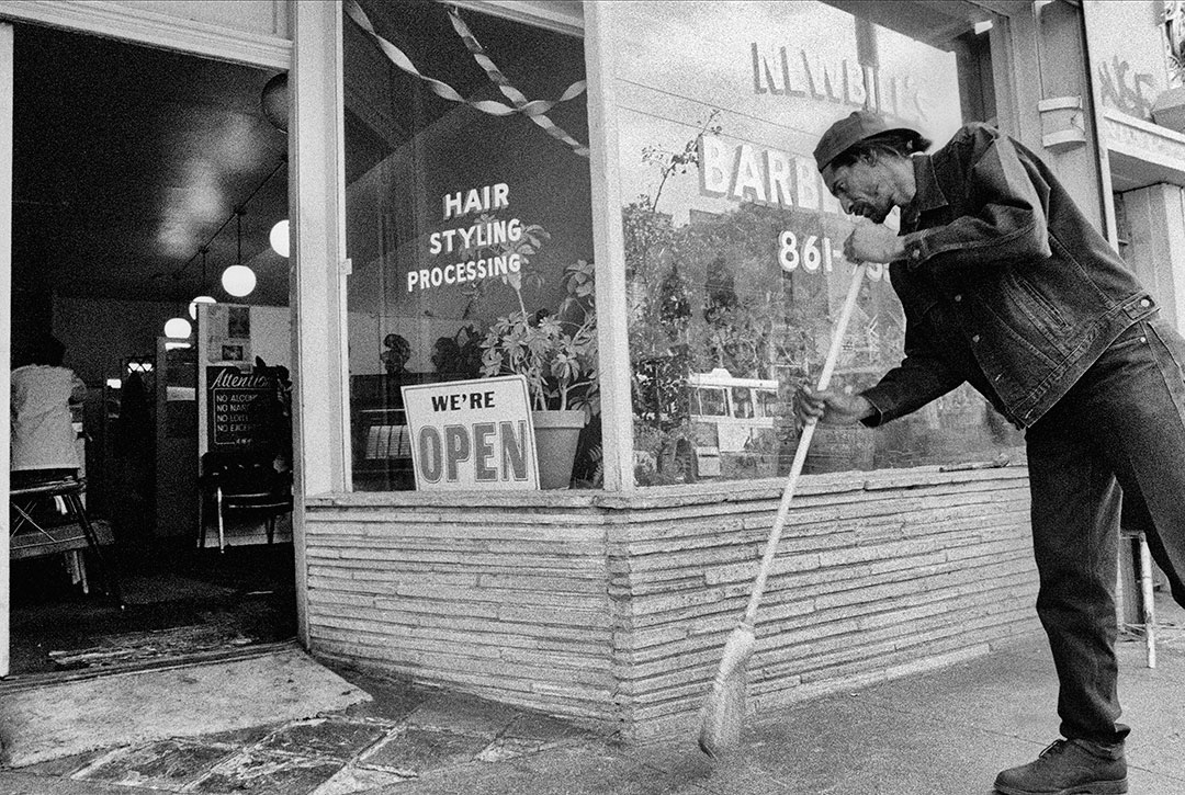 A barber is sweeping the sidewalk in front of his San Francisco shop, 1994.