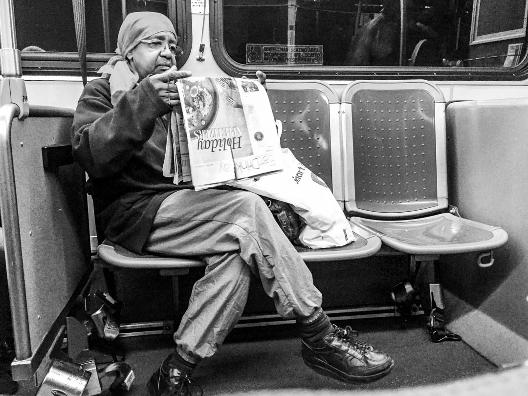 A woman reads a newspaper on an Oakland, California bus, 2017.